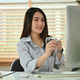 Pleasant asian female entrepreneur holding cup of coffee and reading business email laptop - PhotoDune Item for Sale
