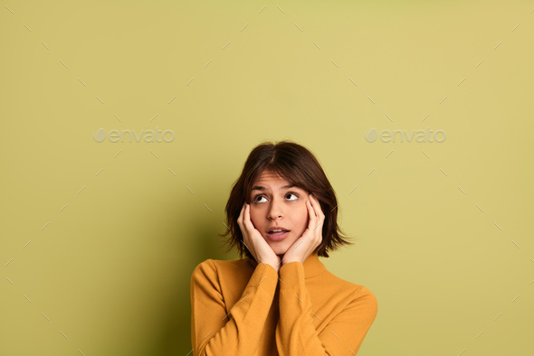 Dreamy young ethnic lady with hands on cheeks looking away in studio - Stock Photo - Images