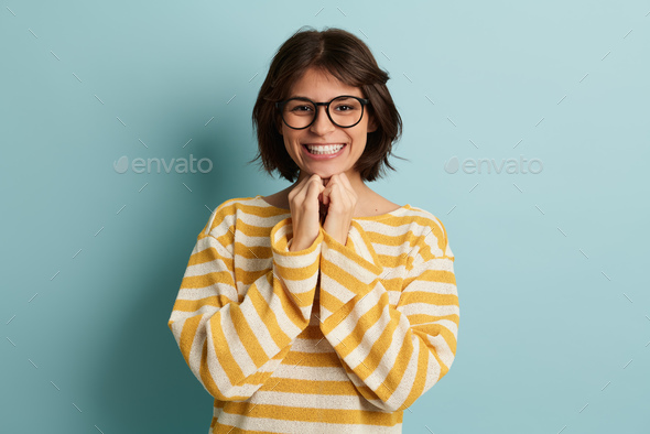 Cheerful female in eyeglasses looking at camera in blue studio - Stock Photo - Images