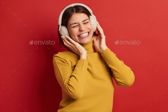 young ethnic woman listening to music in wireless headphones in red studio - Stock Photo - Images