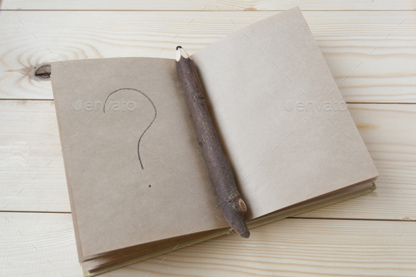 Open notebook with craft paper sheets with question mark on wooden background