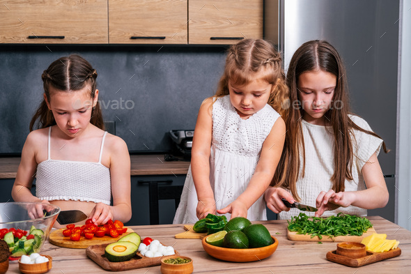 Three cute little sisters preparing vegetarian salad at the kitchen. - Stock Photo - Images