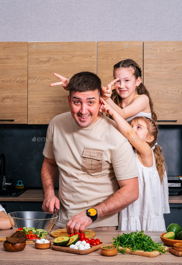 A young father cooks in the kitchen with his little daughters  - Stock Photo - Images