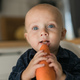 Happy baby sitting in high chair eating carrot in kitchen . Healthy nutrition for kids. Bio carrot - PhotoDune Item for Sale
