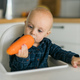 Happy baby sitting in high chair eating carrot in kitchen copy space. Healthy nutrition for kids - PhotoDune Item for Sale