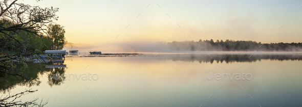Panorama of a calm northern Minnesota lake and fog at dawn during spring with docks along the shore - Stock Photo - Images