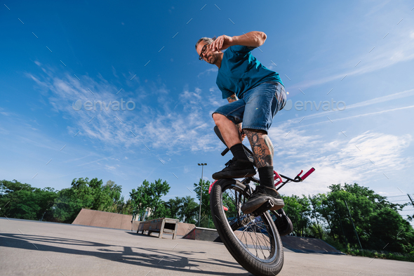 Middle-aged tattooed man is performing freestyle bmx tricks in a skate park and doing extreme sports