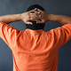 Back view of prisoner in orange t-shirt holding his hands behind his head, surender position  - PhotoDune Item for Sale