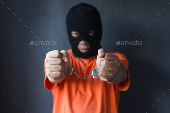 Prisoner in black mask and orange uniform wearing handcuffs clenching ...