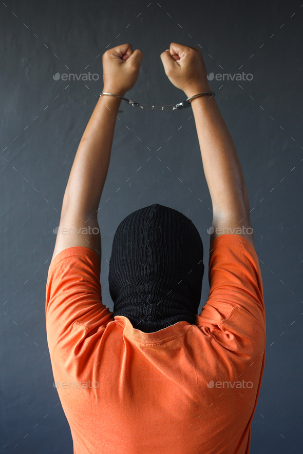 Back view of prisoner in orange t-shirt raise his hands up while in handcuffs over grey wall - Stock Photo - Images
