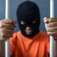A prisoner in orange shirt and black mask inside the bars of a prison  - PhotoDune Item for Sale