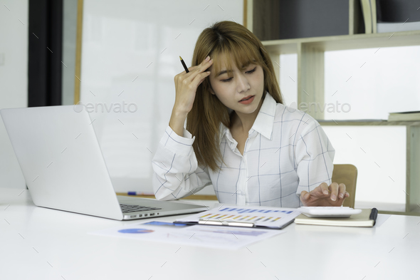Worried bookkeeper, Asian female finance calculating on a calculator sitting on a desk at the office