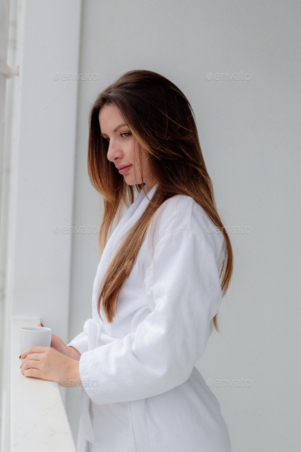 Relaxed Asian woman wearing bath robe drinking coffee in hotel room in morning - Stock Photo - Images