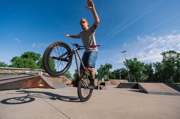 A middle aged active man is performing tricks on in a skate park on his bmx bike.