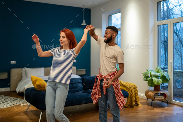 Happy romantic multiracial young couple in love learning to dance together at home - Stock Photo - Images