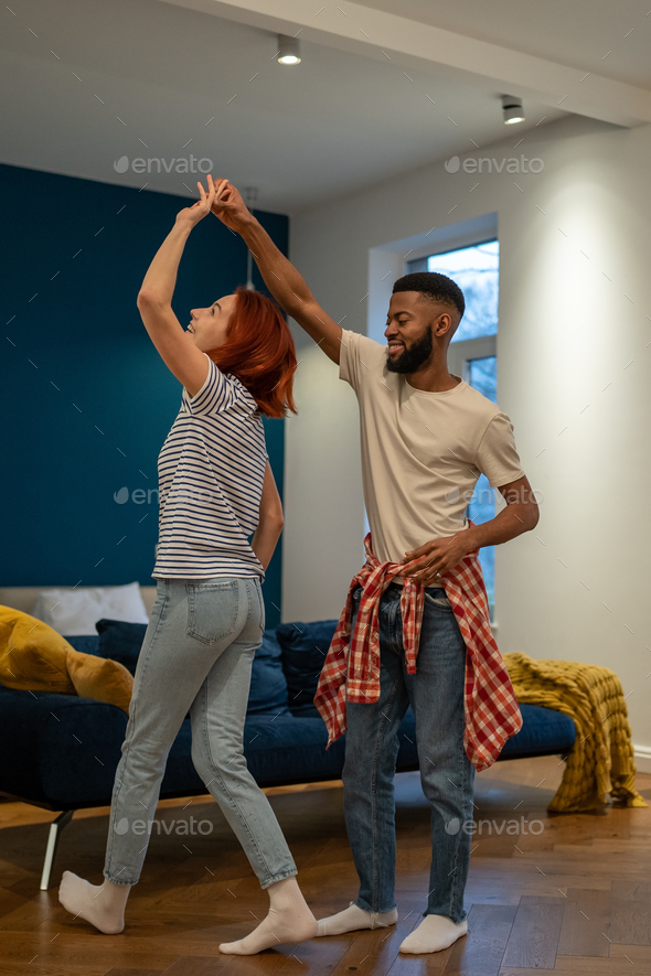 Loving young diverse couple dancing romantic dance in modern bedroom with panoramic windows.