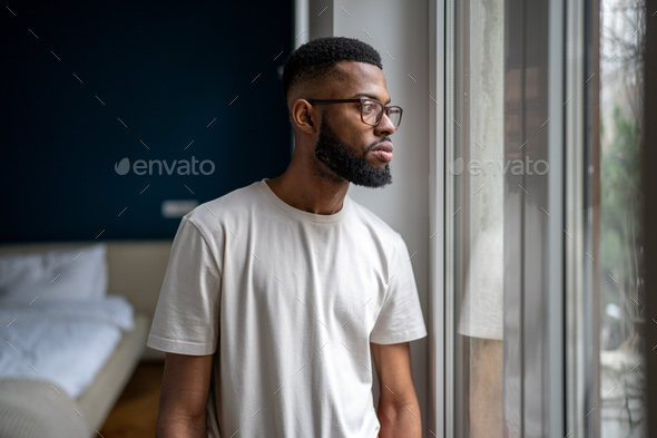 Sad Black man looking out of window thinking about life problems, dealing with breakup depression