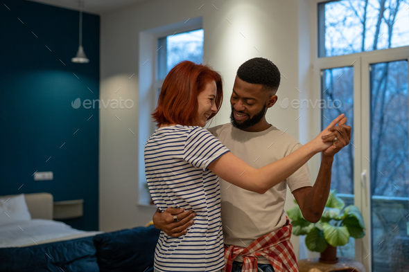Joyful young diverse married couple dancing having fun in living room at home - Stock Photo - Images