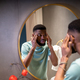 Worried african american man looks at mirror, touches facial skin anxious about wrinkles. - PhotoDune Item for Sale