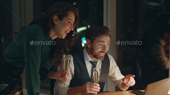 Two partners celebrating victory with champagne looking at laptop late night. - Stock Photo - Images