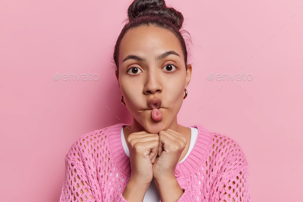 Funny young Latin woman with dark hair puckers lips keeps hands under chin  makes fish face funny Stock Photo by wayhomestudioo