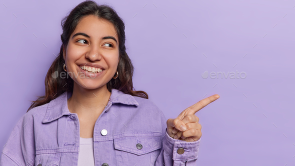 Beautiful cheerful woman smiles broadly points index finger shows copy space ideal for advertising - Stock Photo - Images