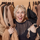 Cheerful surprised young blonde woman stares impressed poses among stylish clothes hanging on rail - PhotoDune Item for Sale