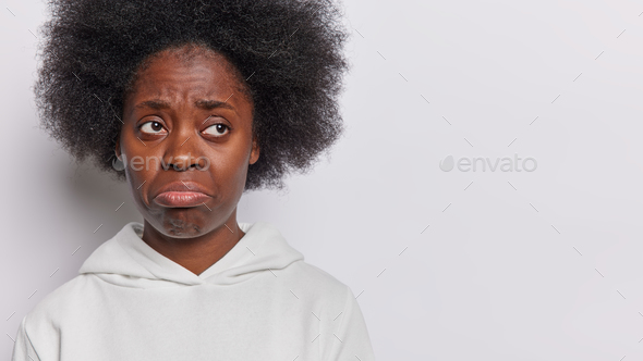 Studio shot of Afro woman with bushy hair purses lips and feels dissatisfied has sulking expression - Stock Photo - Images