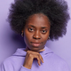 Portrait of dark skinned woman with curly bushy hair keeps hand under chin focused attentively at - PhotoDune Item for Sale