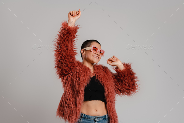 Happy young short hair woman in trendy clothes dancing against grey background - Stock Photo - Images