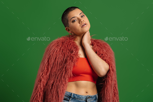 Fashionable short hair woman in fluffy jacket looking at camera against green background - Stock Photo - Images