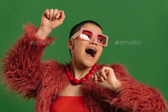 Happy young short hair woman in trendy clothes dancing against green background - Stock Photo - Images