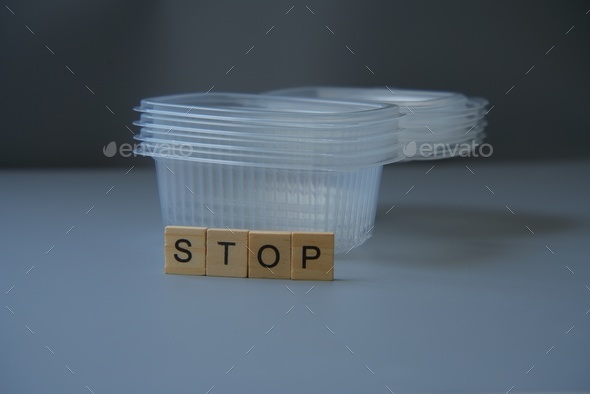 A stack of plastic food containers with the word \'Stop\' written in wooden letters placed on top