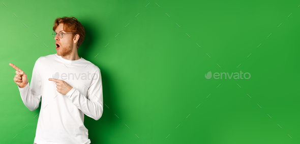 Impressed redhead man in glasses checking out promo, pointing and looking left with amazed face - Stock Photo - Images