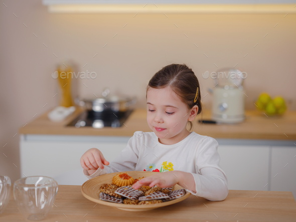 Happy little baby girl smiles happily when she eats cookies - Stock Photo - Images