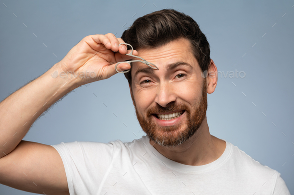 Portrait of handsome middle aged man plucking his eyebrows, using tweezers for brows correction