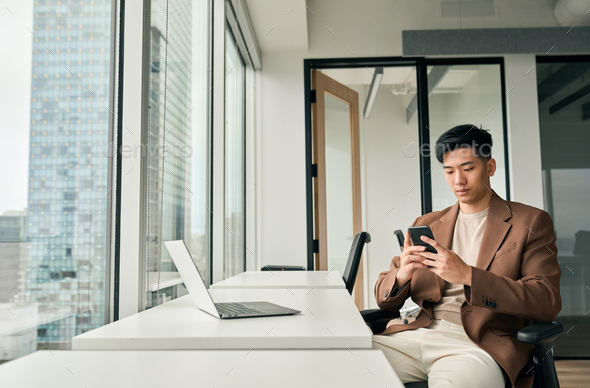 Young busy Asian business man working using mobile and laptop in office. - Stock Photo - Images