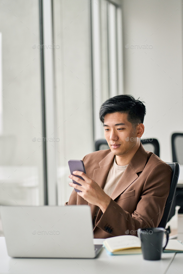 Young busy smiling Asian business man using mobile phone in office. - Stock Photo - Images