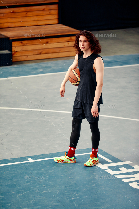 Sports guy on the basketball court, a guy with long hair trains with the ball on the basketball