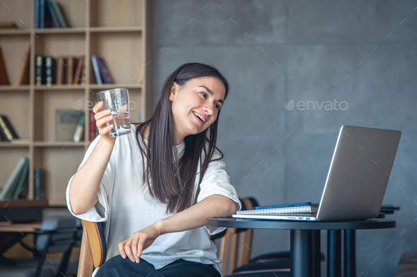 Young woman with a glass of water in front of a laptop. - Stock Photo - Images