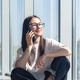 A young woman in glasses is talking on a smartphone near the window. - PhotoDune Item for Sale