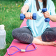 Woman stretching with dumbbells, doing fitness exercises in green park. - PhotoDune Item for Sale