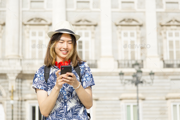 Young with backpack and hat, smiling and happy, using mobile phone - Stock Photo - Images