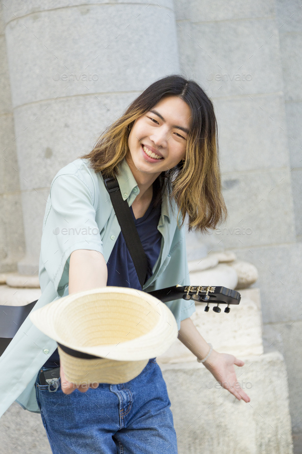 Young street musician happily busking with guitar and hat - Stock Photo - Images