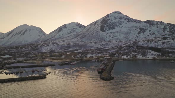 Local fishing boat returns to harbour from arctic waters, sunset snowy mountains alt