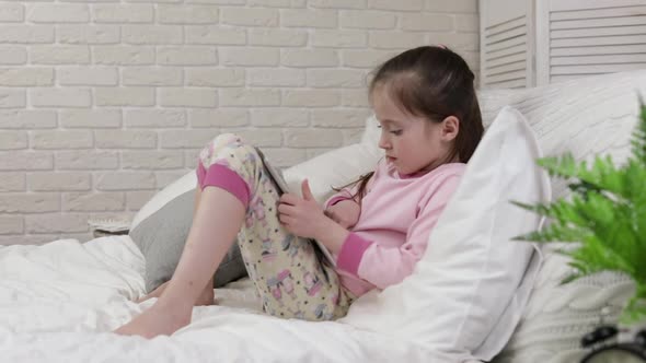 Cute Little Child Girl Lies in Bed Uses Digital Tablet