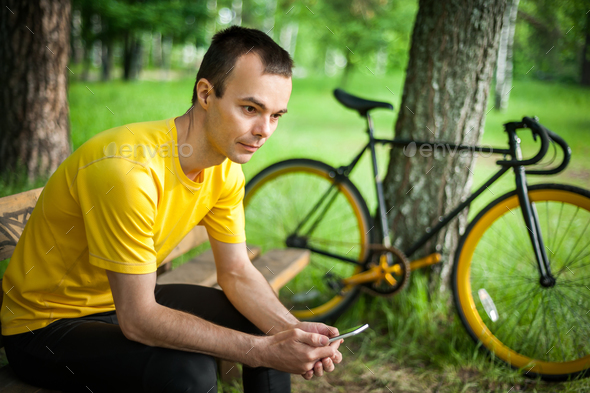 A young man sitting on a bench in a public Park communicates via mobile communication. - Stock Photo - Images