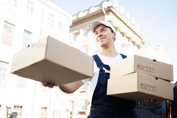 A male courier in the form of a driver delivers an order in boxes of a courier company to the house.