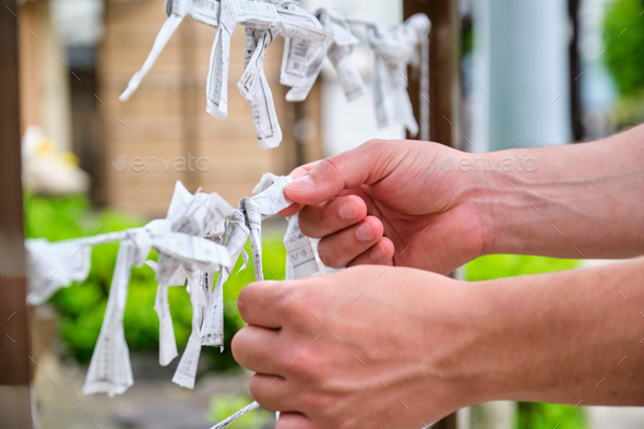 Male hands tying unwanted omikuji up to leave bad luck behind at musubidokoro.