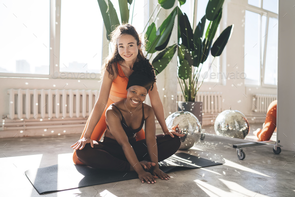 Slim woman in yoga pose on mat and friend helping her in gym Stock Photo by  GaudiLab